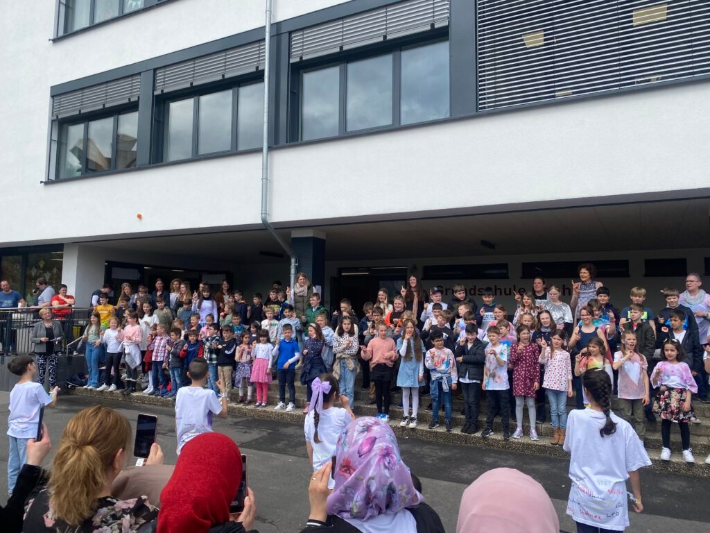 Alle Kinder der Grundschule Cochem stehen vor der Schule und singen.