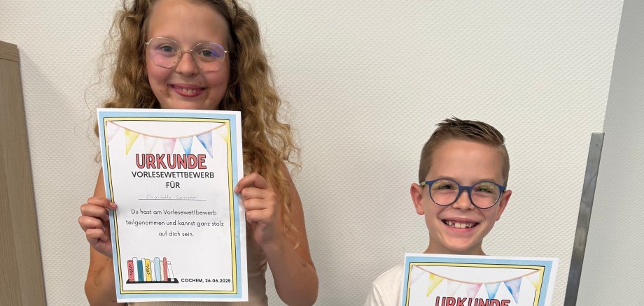 Ein Mädchen und ein Junge halten ihre Urkunde in der Hand.