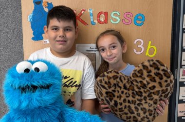 Ein Junge hält das Krümelmonster und ein Mädchen ein großes Stoffherz in den Händen und lächeln